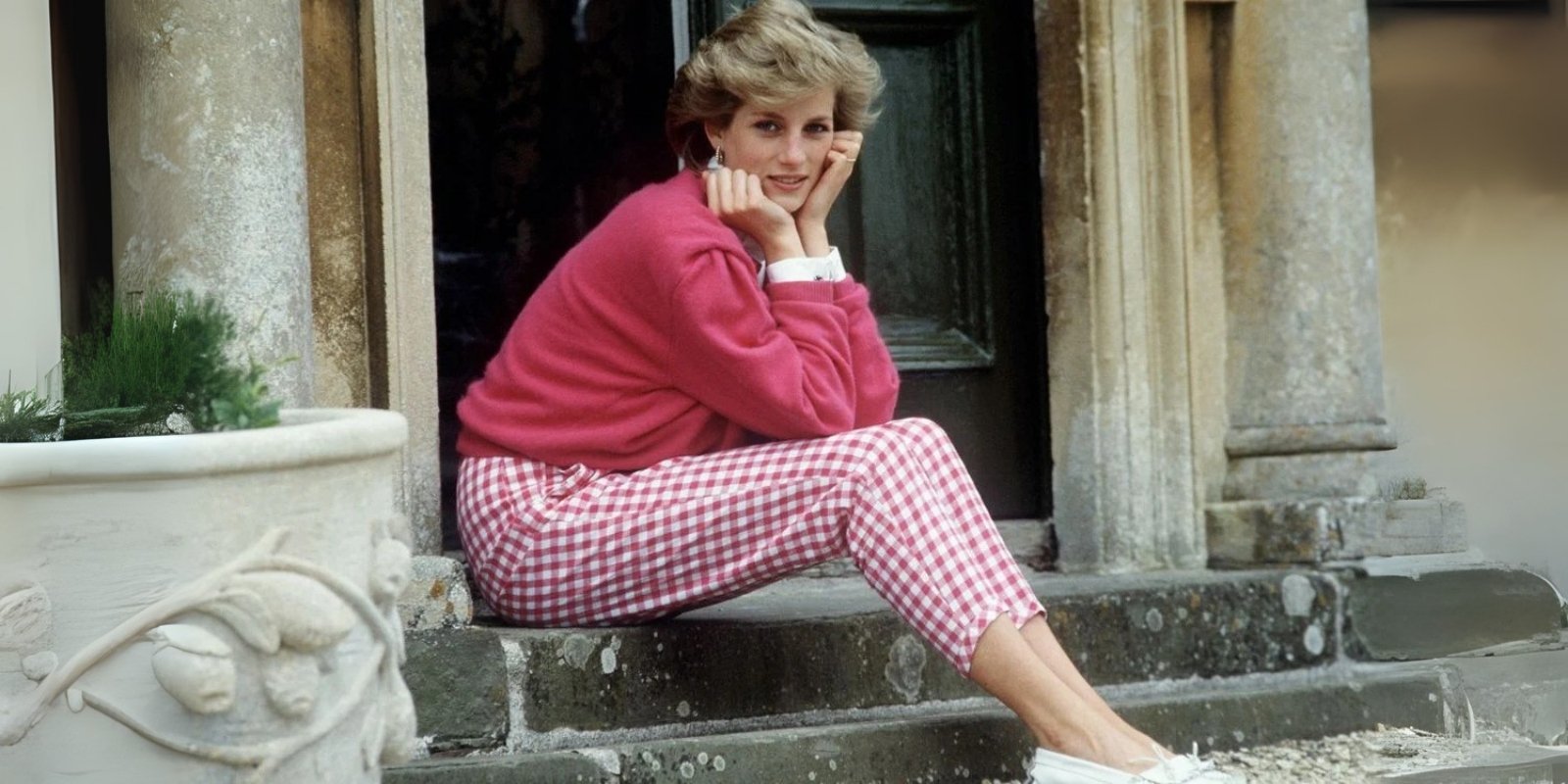 Princess Diana in a pink sweatshirt with pink and white chequered pants sat on the steps